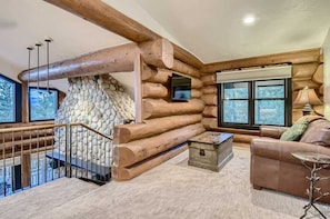 Ein rustikales Blockhaus-Interieur mit Kamin aus Stein, einer Holztreppe, einer Couch und einem Fernseher.