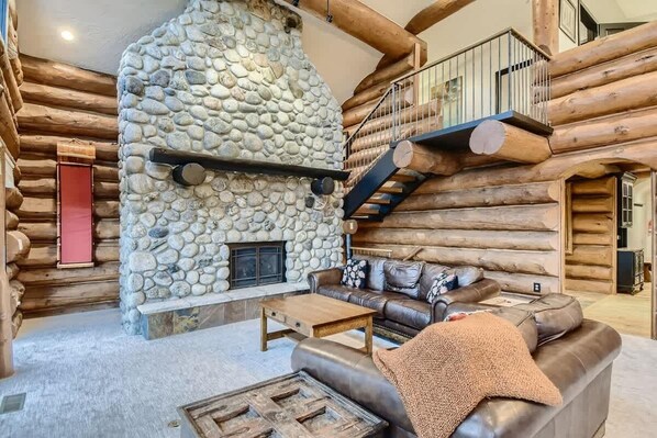 A log cabin interior with a stone fireplace, a leather sofa, and a wooden coffee table.