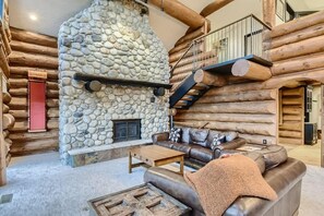 A log cabin interior with a stone fireplace, a leather sofa, and a wooden coffee table. - Private Hot Tub in Amazing Home Away From Home! (Silverthorne)