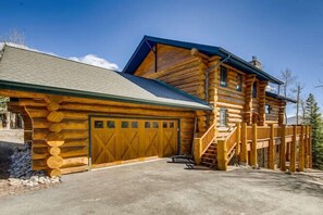 Une cabane en rondins avec un garage, une véranda et un escalier menant à l’étage supérieur.