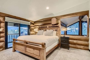 A log cabin bedroom with a wooden bed, a nightstand, and a window with a view of trees.
