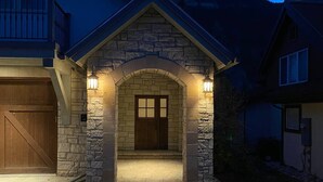 A stone house with a wooden garage door, a stone entrance, and two wall-mounted lights.