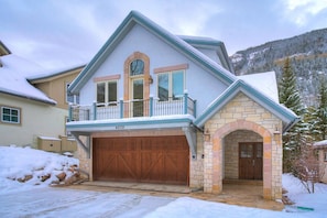 A two-story house with a stone entrance, a wooden garage door, and a balcony with a railing. - 🏆 East Vail Home | 4 En-Suite Bedrooms | Heated Garage | Bus to Vail Village (Vail)