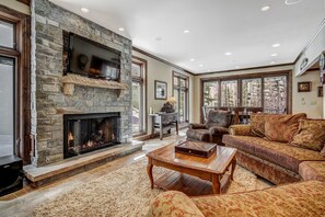 A spacious living room with a stone fireplace, comfortable seating, and large windows offering a view of the outdoors. - 🏆 East Vail Home | 4 En-Suite Bedrooms | Heated Garage | Bus to Vail Village (Vail)