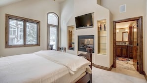 A bedroom with a large bed, a fireplace, and a TV mounted on the wall.