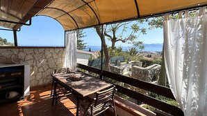En balkon med et bord og stole, en stenvæg og havudsigt.