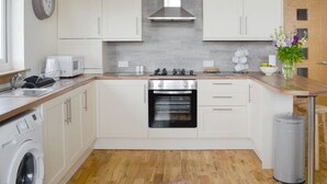 A modern kitchen with white cabinets, a stainless steel range hood, a built-in oven, and a washing machine.