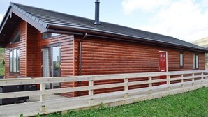 A wooden cabin with a metal roof, a chimney, and a wooden deck.