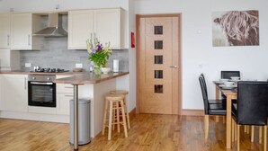 A modern kitchen with white cabinets, a built-in oven, and a wooden dining area with a table and chairs.