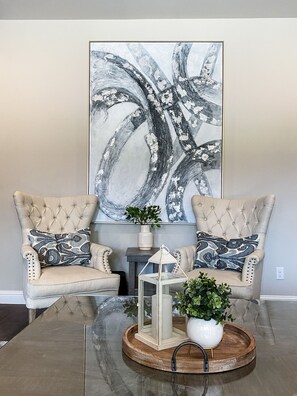 Relax in a stylish space with tufted armchairs, a large abstract painting, and a glass coffee table.