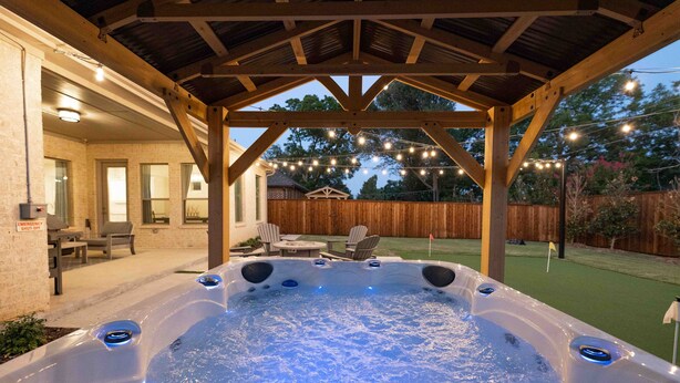 A hot tub under a wooden pergola with string lights, surrounded by a patio area with chairs and a table. - Entertainment District: Game Room Hot Tub Putting Green 4 Baths Walk to Stadiums (Arlington,)