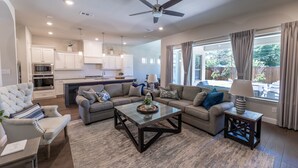 A modern living room with a glass coffee table, sofas, and a dining area with a kitchen in the background. - Entertainment District: Game Room Hot Tub Putting Green 4 Baths Walk to Stadiums (Arlington,)