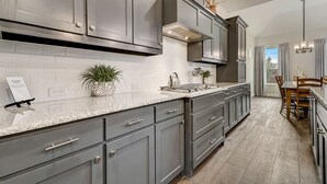 A modern kitchen with grey cabinets, a granite countertop, and a dining area with a wooden table and chairs.
