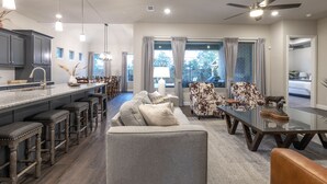 A modern kitchen with a bar area, a dining table, and a living room with a sofa and chairs.