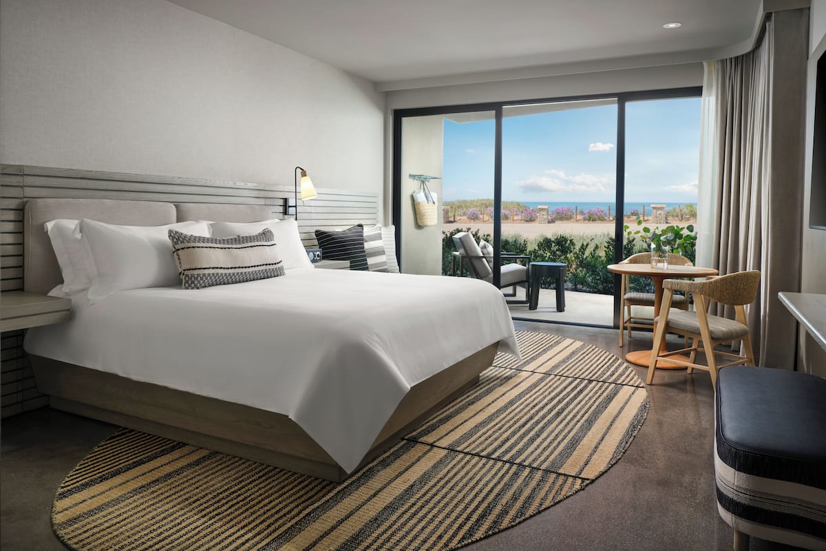 A modern hotel room with a large bed, a balcony with a view, and a small seating area.