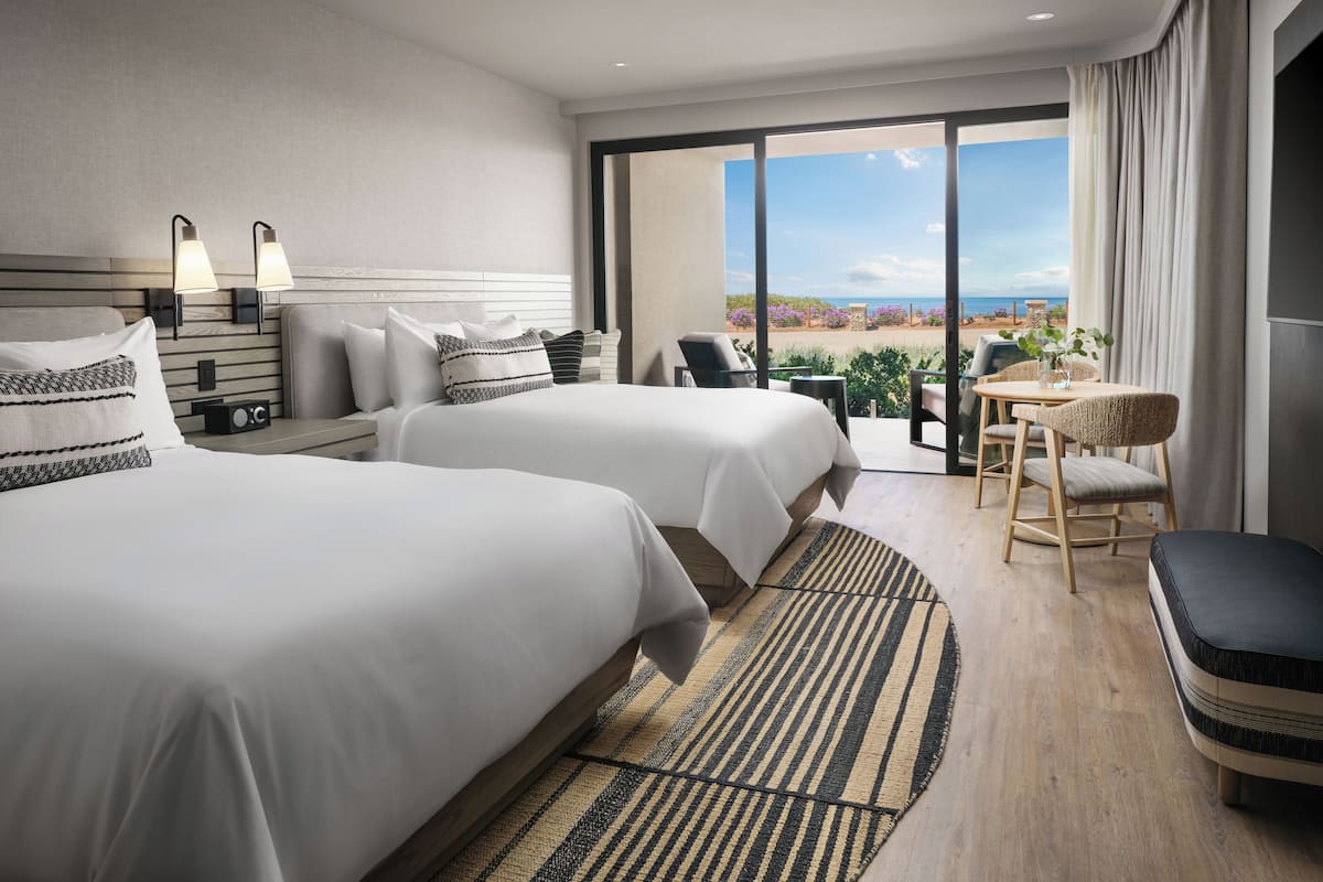 A hotel room with two beds, a sitting area with a table and chairs, and a view of the beach.