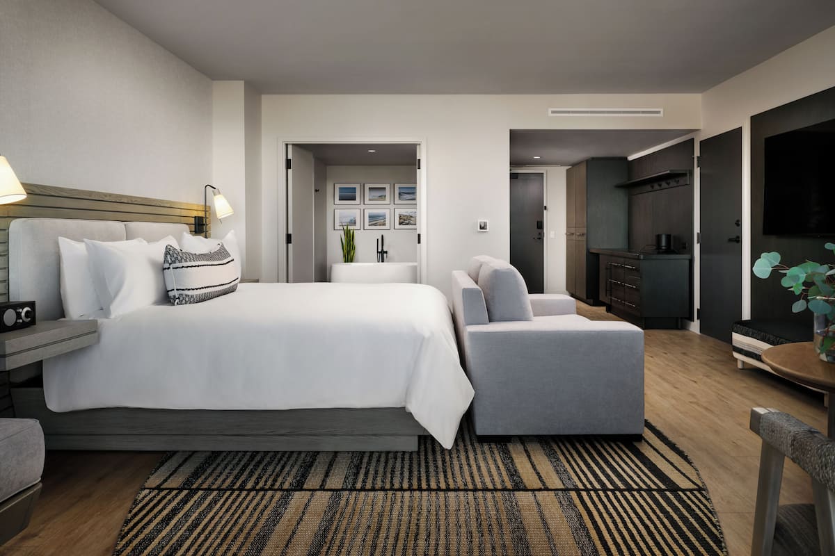 A modern hotel room with a large bed, a sofa, a desk, and a TV.