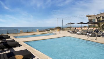 A pool area with lounge chairs, a small table, and umbrellas, overlooking the ocean.