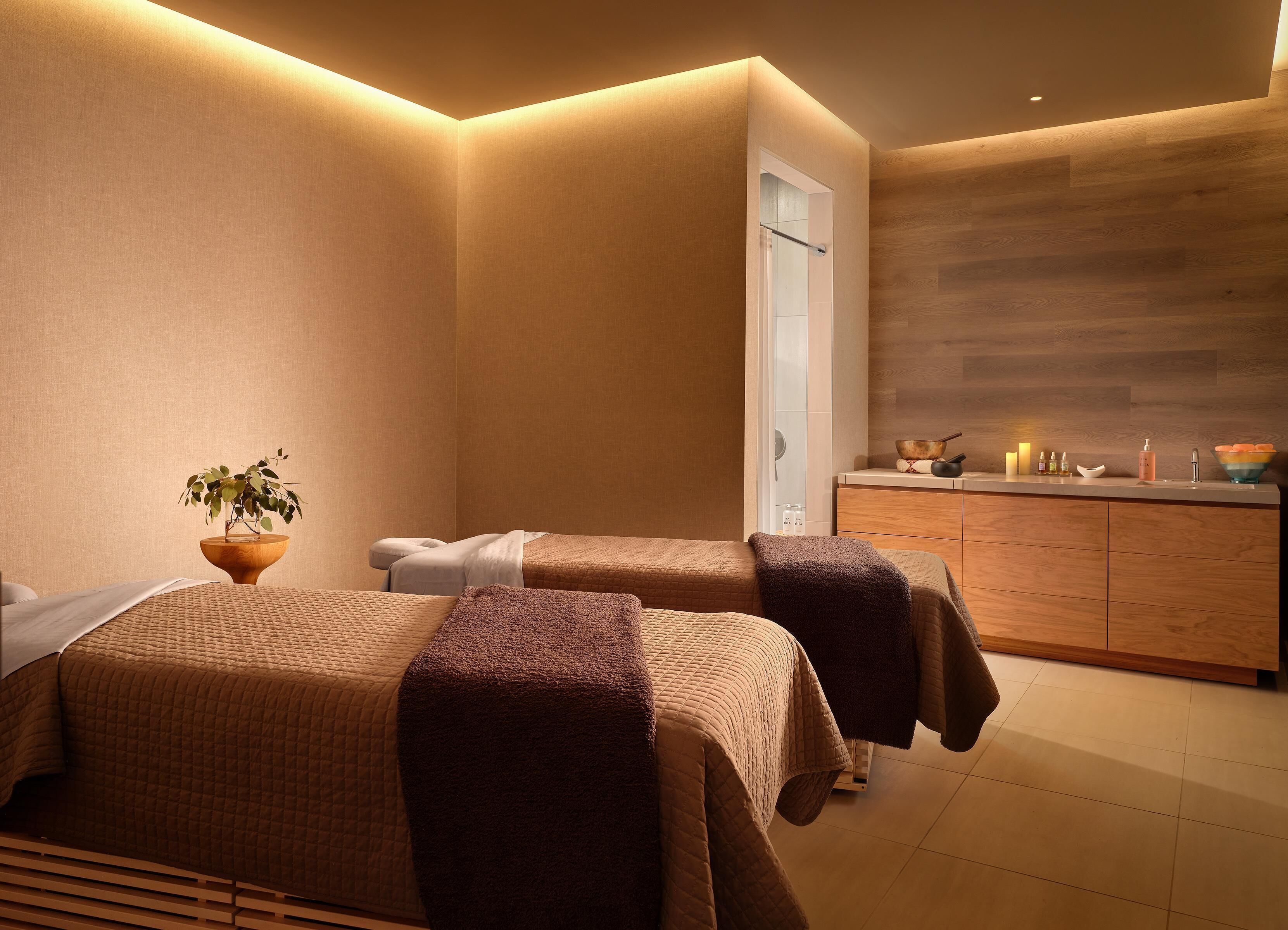 A spa room with two beds, a wooden cabinet, and a small plant.