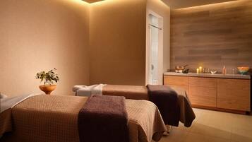 A spa room with two beds, a wooden cabinet, and a small plant.