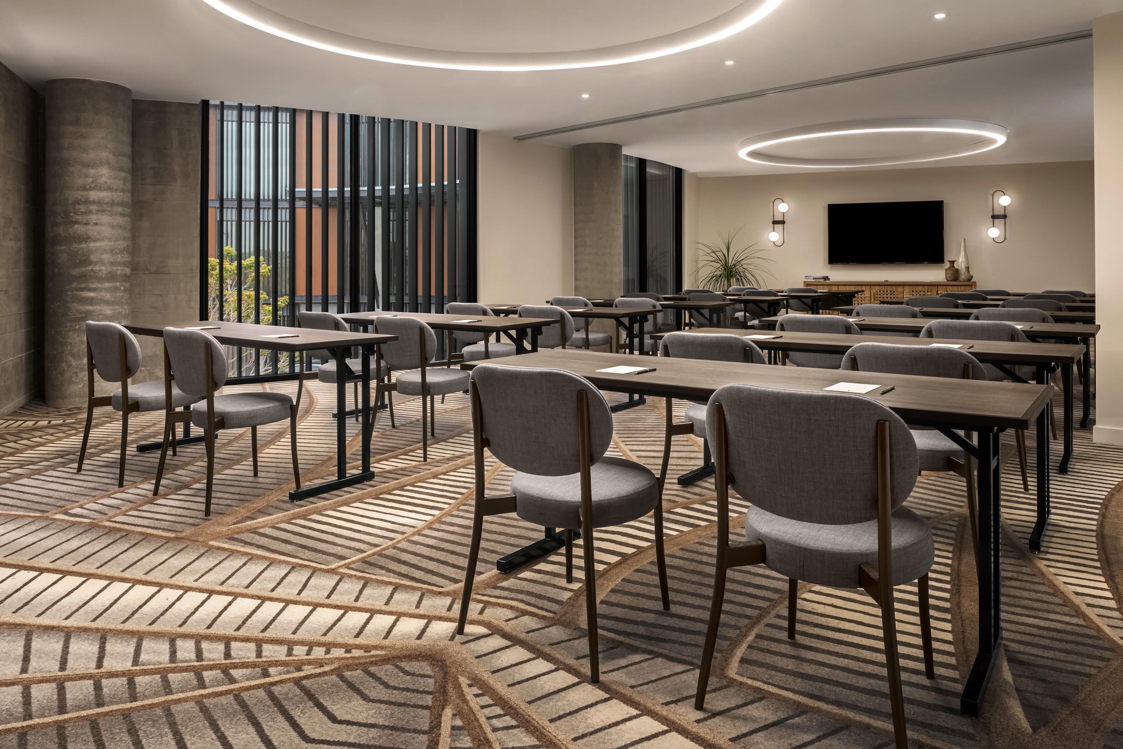 Une salle de conférence équipée de tables et de chaises, d’un grand écran et d’un tapis à motifs.