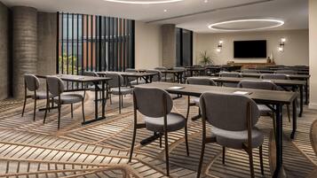 Une salle de conférence équipée de tables et de chaises, d’un grand écran et d’un tapis à motifs.