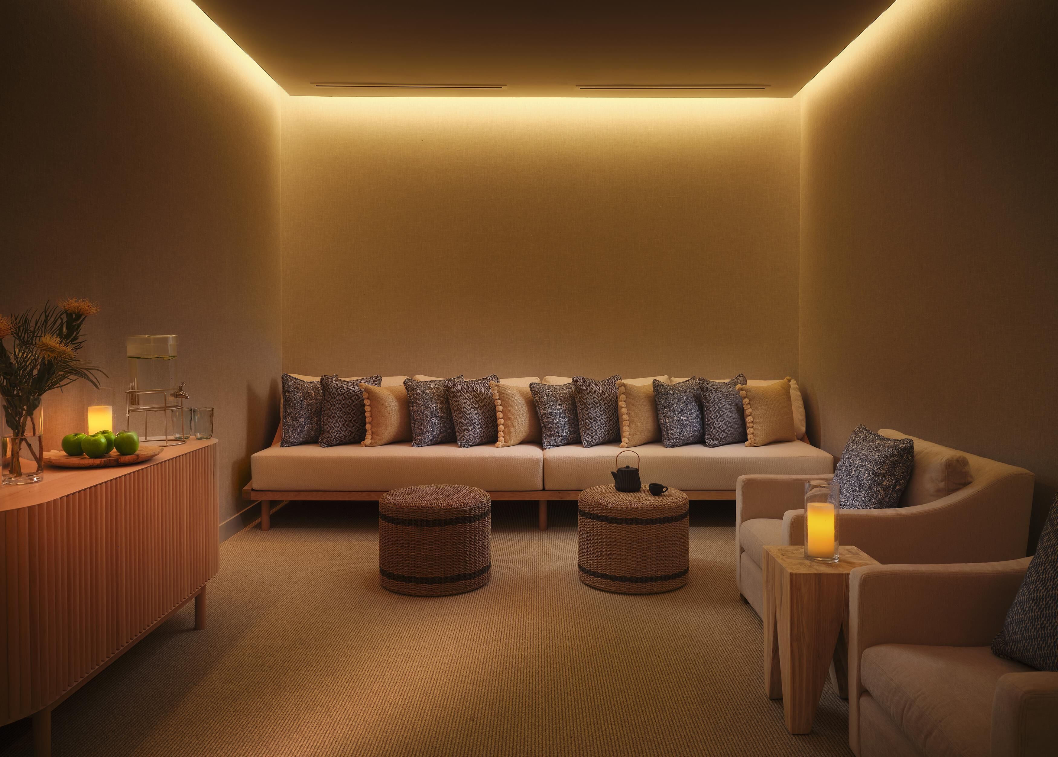 A cozy lounge area with a sofa, two ottomans, a small table, and a vase with green apples.