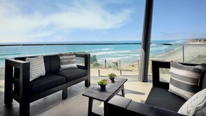 Un balcon avec vue sur l’océan, un canapé, une petite table avec une plante et un plafond en bois.