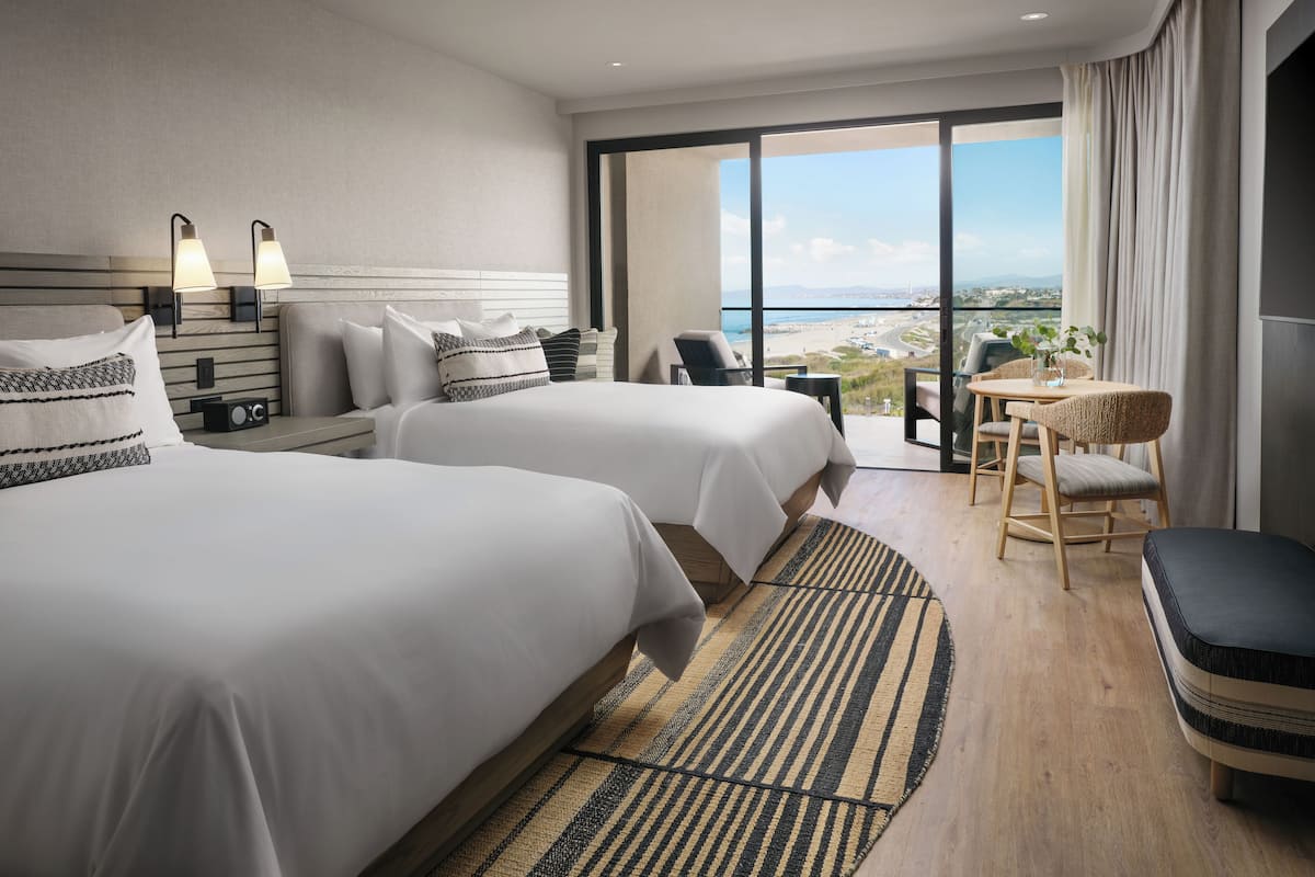 A hotel room with two beds, a small table with chairs, and a view of the beach.