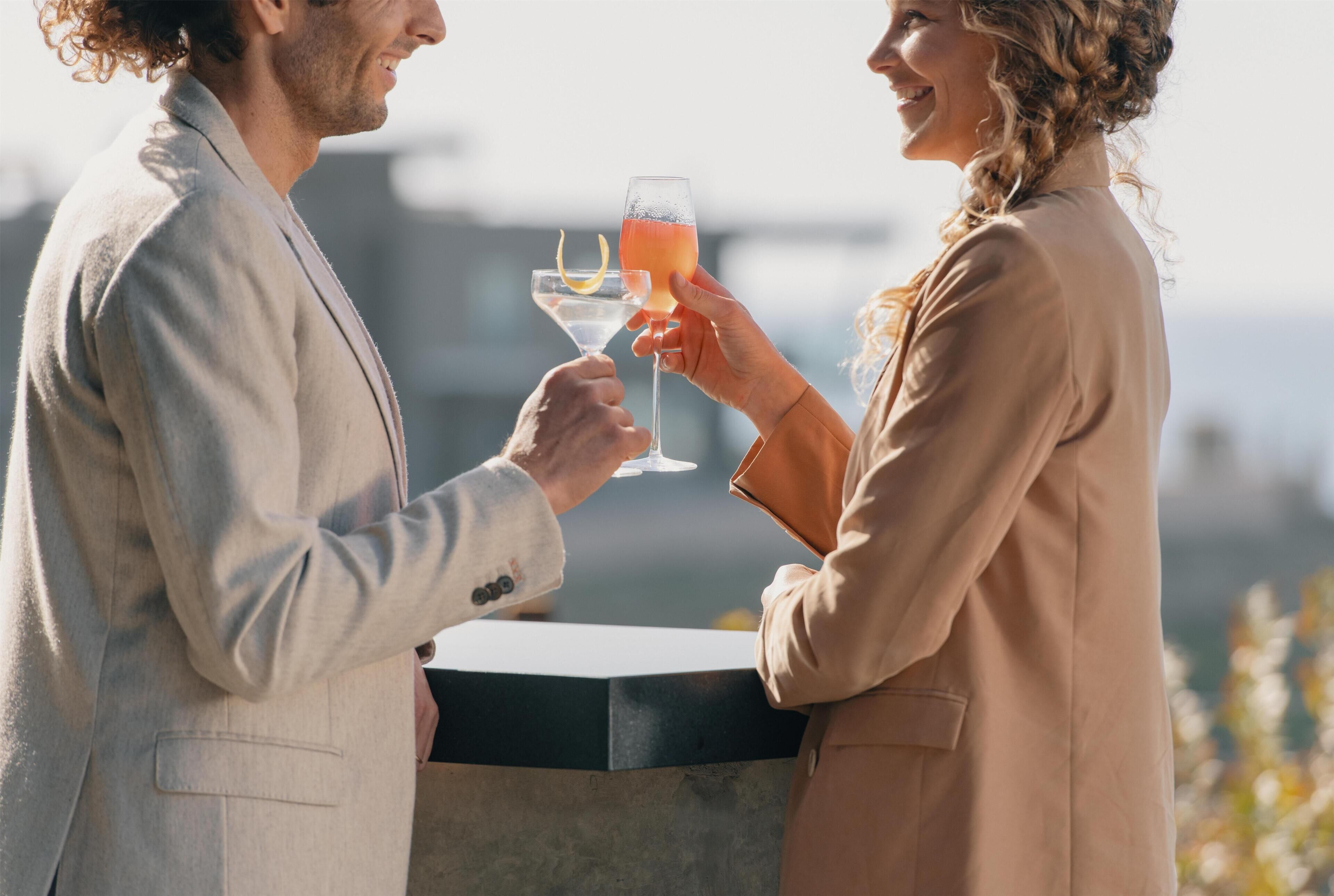 Two people holding drinks at a bar with a view.