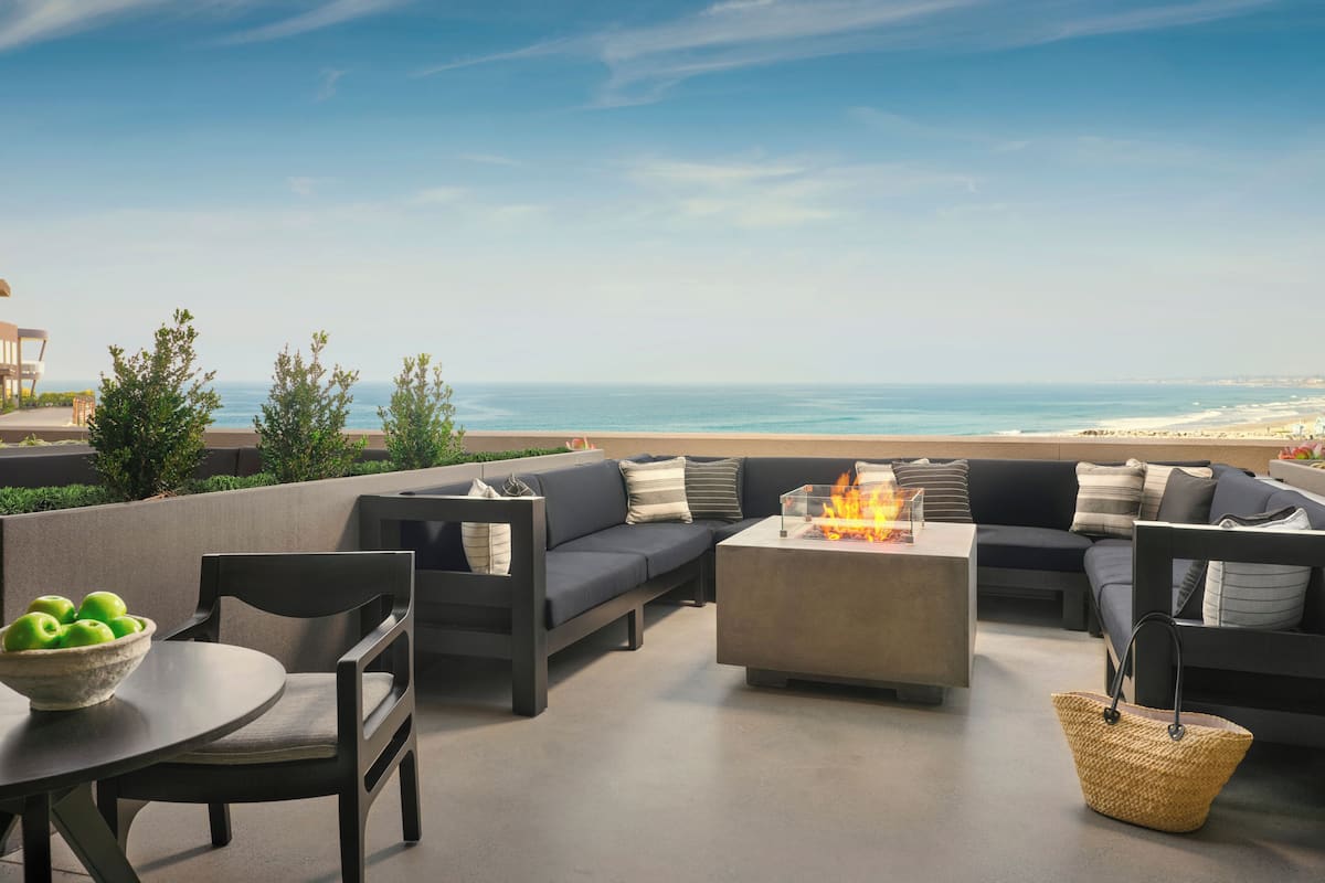 A rooftop terrace with a sofa set, a table with a bowl of apples, and a fire feature.