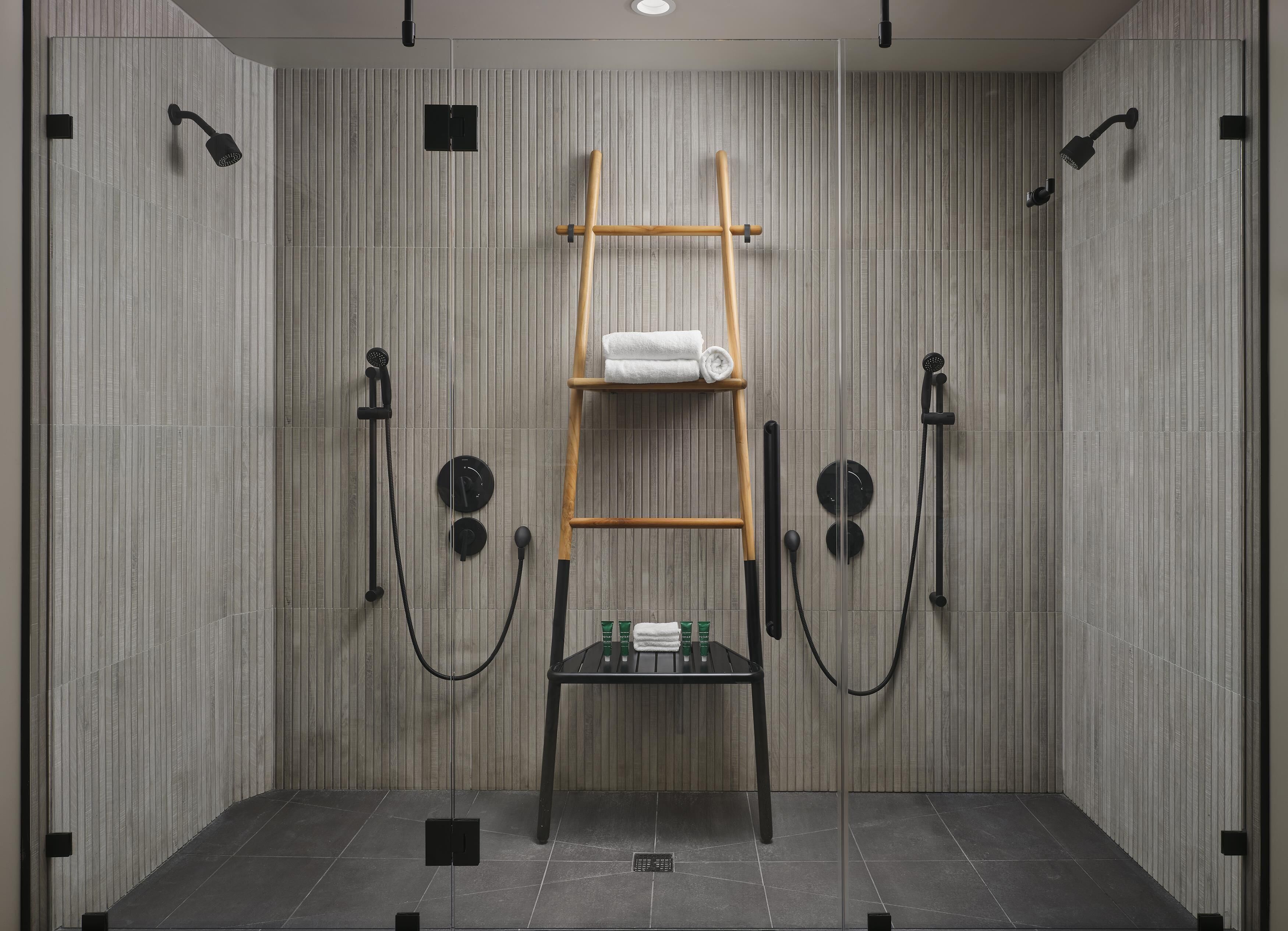 A modern bathroom with a vertical panel wall, a wooden ladder, a towel rack, and two handheld showerheads.