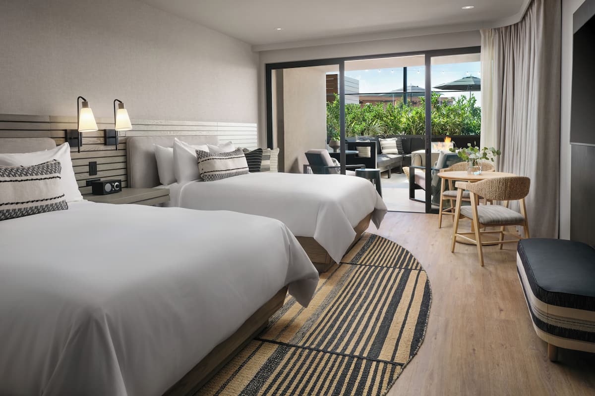 A hotel room with two beds, a sofa, a dining table, and a view of greenery outside.