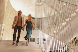 A man and woman walking down a spiral staircase with a modern design and glass railings.
