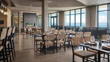 A spacious dining area with high tables and chairs, large windows, and a fireplace.