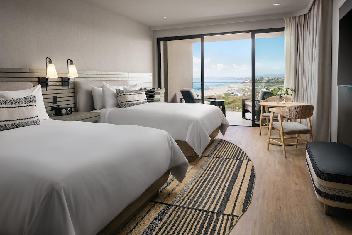 A hotel room with two beds, a dining area, and a view of the beach.