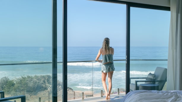 A room with a large window overlooking the ocean, a bed, and a chair.