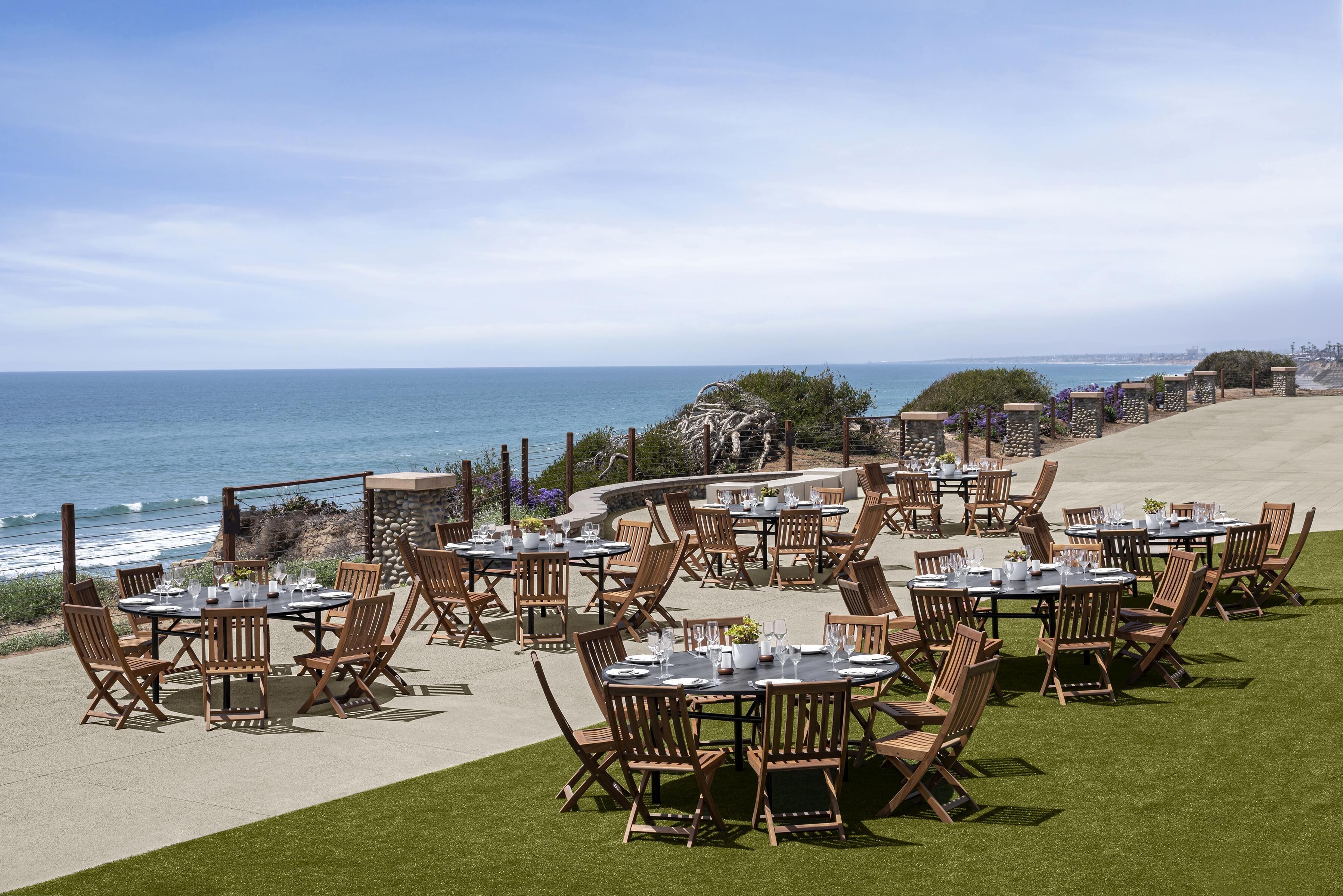 An outdoor dining area with tables and chairs, overlooking the ocean.