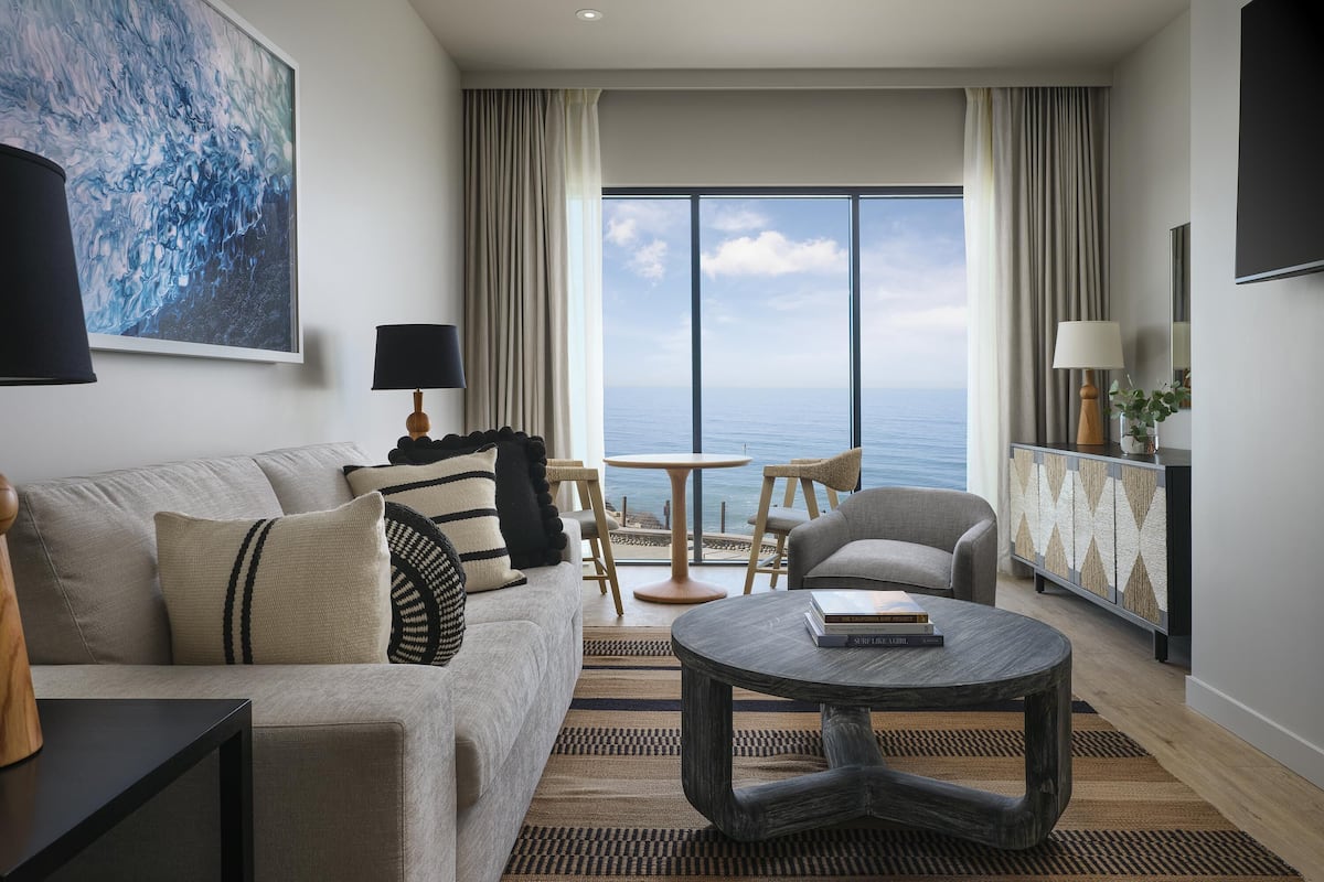 A modern living room with a sofa, armchairs, a coffee table, and a view of the sea.