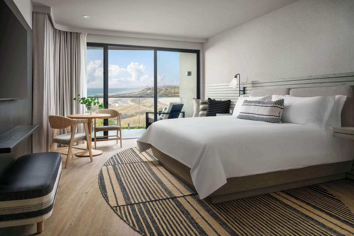 A hotel room with a large bed, a desk, a chair, and a view of the beach.