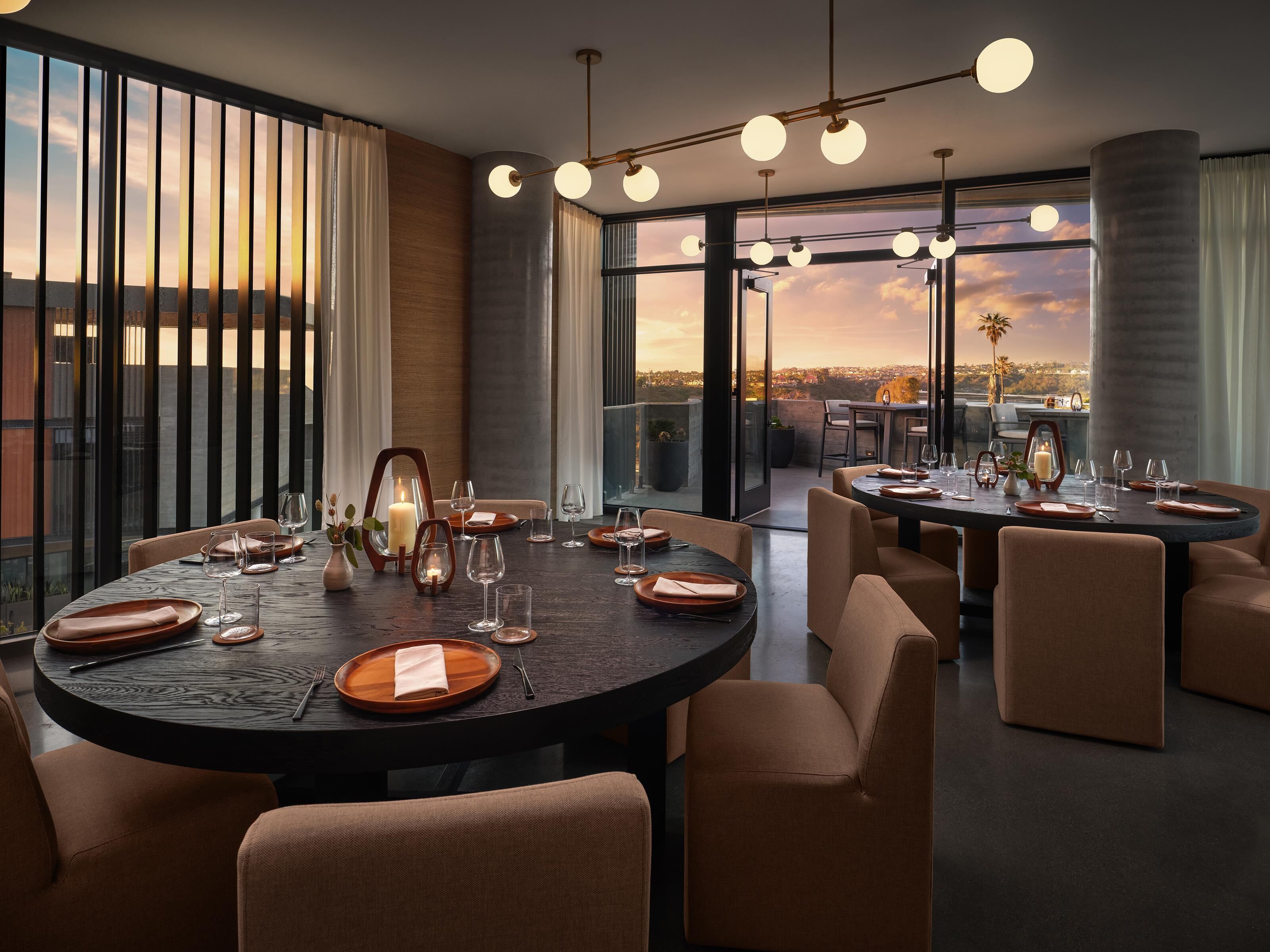 Un comedor moderno con mesas redondas, sillas y vista a la ciudad.