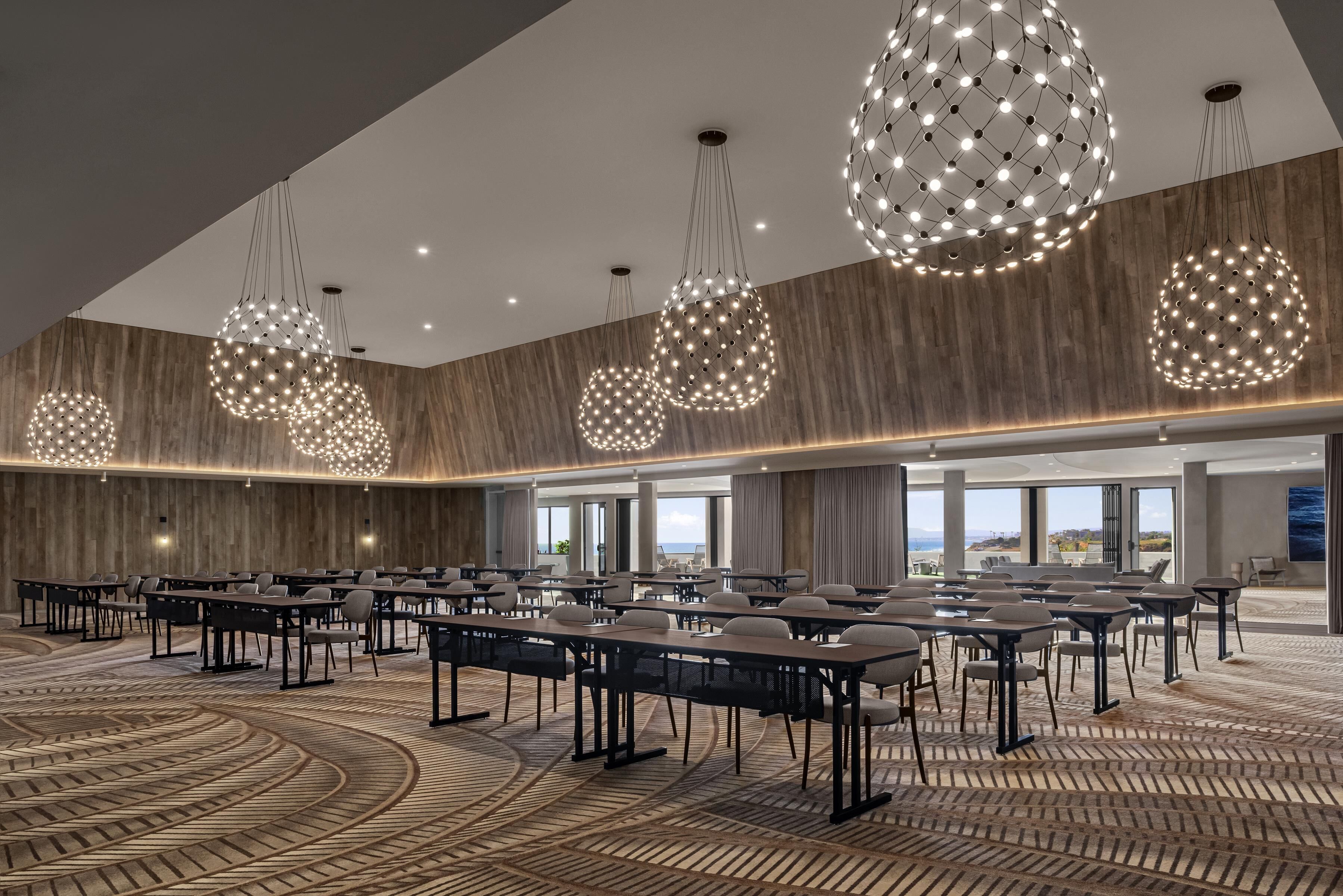 A conference room with round tables and chairs, large spherical hanging lights, and a wooden wall.