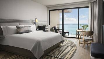 A modern hotel room with a large bed, a sitting area with a view, and a balcony overlooking the sea.