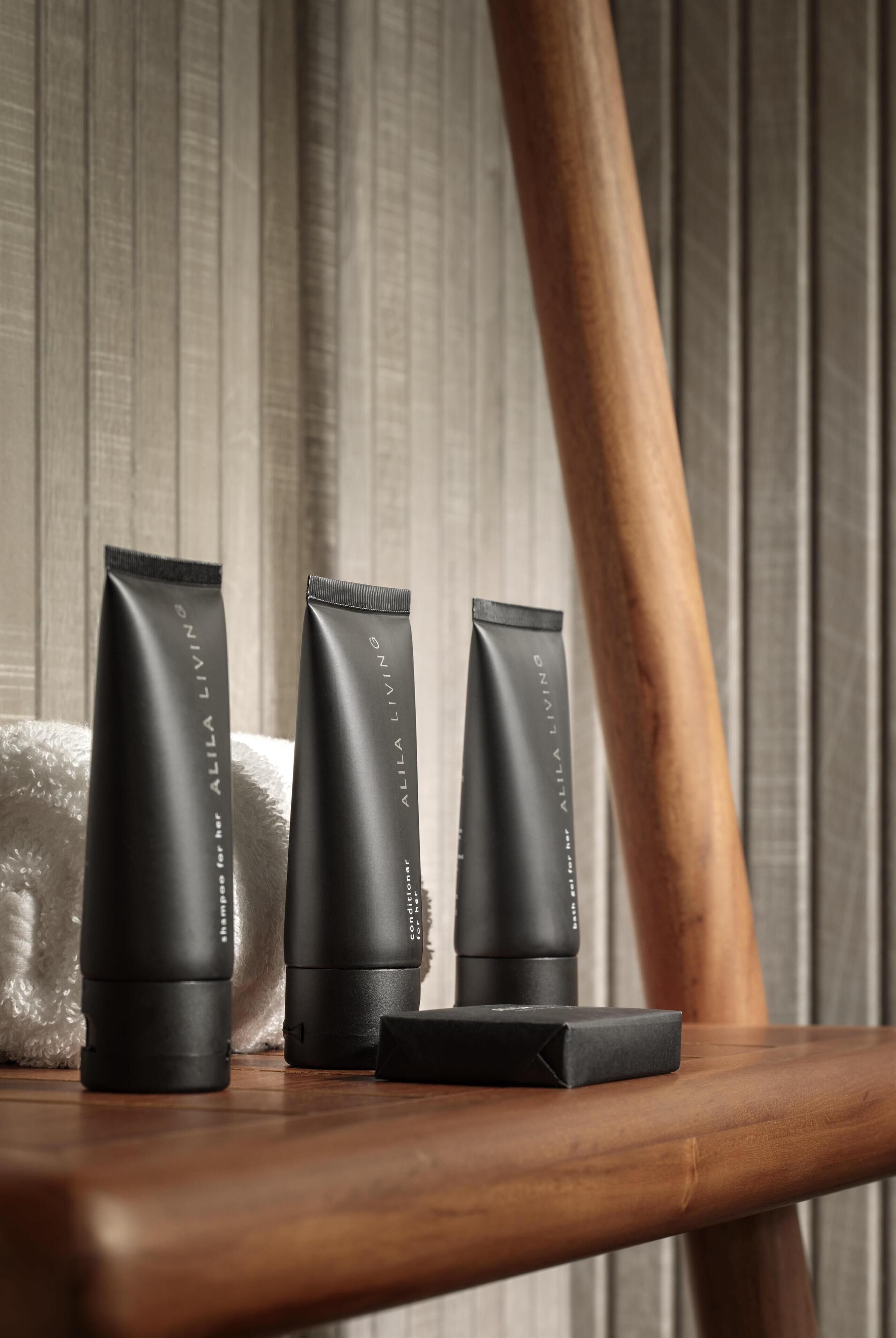 Three black tubes of Alila Living on a wooden surface with a towel in the background.