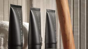 Three black tubes of Alila Living on a wooden surface with a towel in the background.