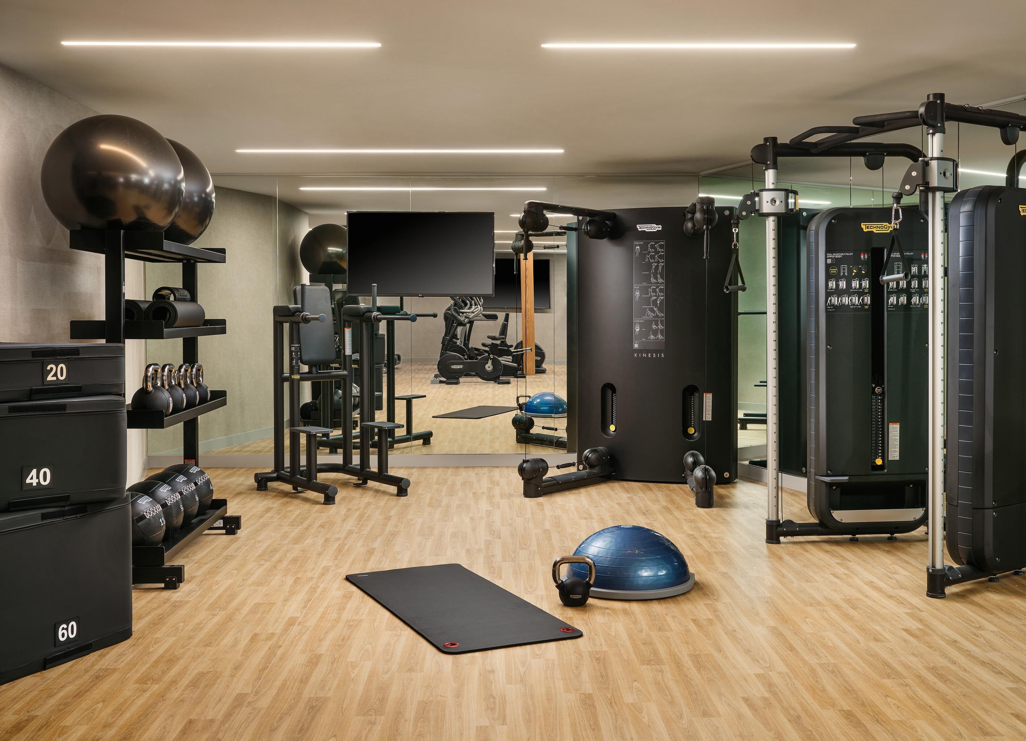 A gym with exercise equipment, a wooden floor, and a black mat.