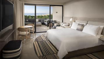 Habitación de hotel con una cama grande, televisor, zona de estar con mesa y sillas, y vistas al exterior.