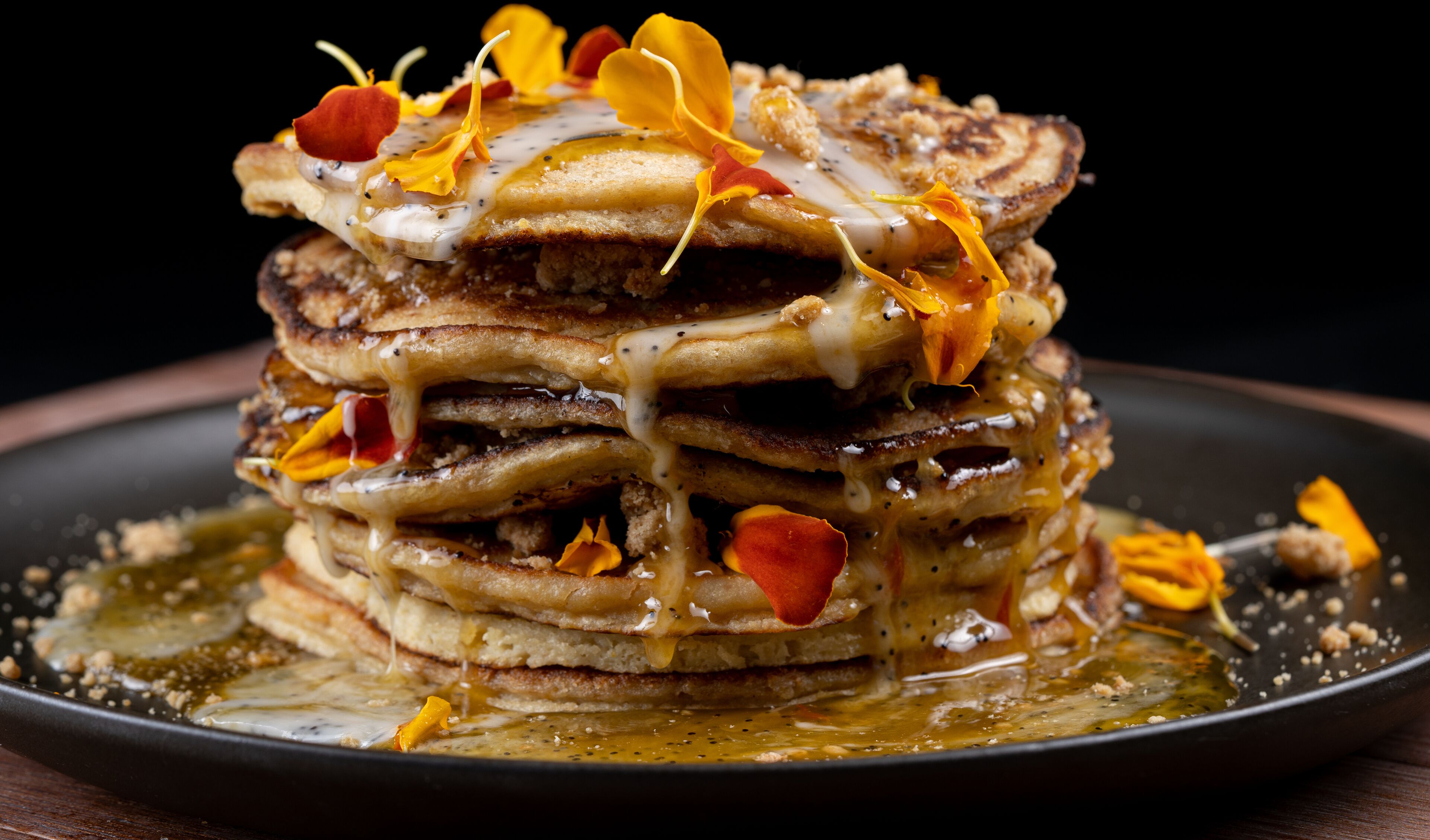 A stack of pancakes with syrup and edible flowers on a plate.