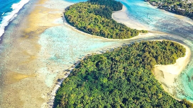 Vista aérea de una isla tropical con aguas turquesas cristalinas, playas de arena y vegetación verde exuberante.