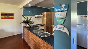 Una cocina con un armario de madera, un fregadero y una estufa. Hay un cartel en la pared que dice "Rarotonga es mi lugar feliz".